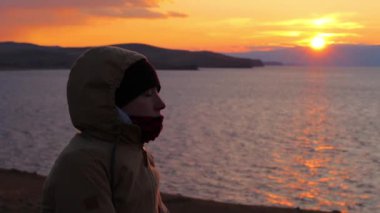 Kız deniz kıyısında oturur ve derin derin düşünür. Güzel altın gün batımı