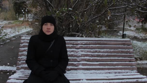 Portré egy lány, egy fekete ruhás, ül egy padon a parkban, télen — Stock videók