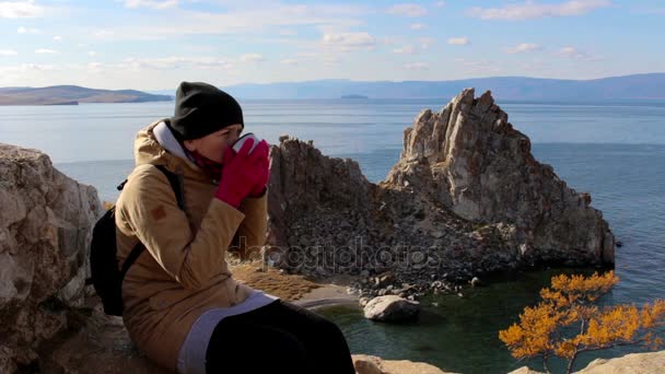 Το κορίτσι που κάθεται πάνω σε ένα βράχο δίπλα στη θάλασσα με φόντο καταπληκτικό τοπίο, ποτά τσαγιού — Αρχείο Βίντεο