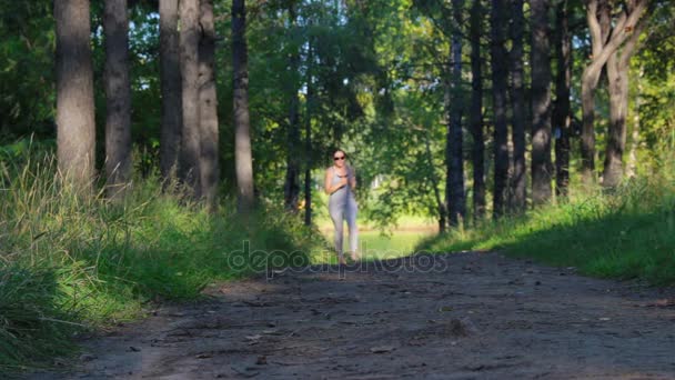 Девушка бежит по темно-зеленой аллее леса. Молодая женщина бегает в парке — стоковое видео