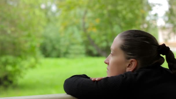 Närbild av en fundersam tjej med en drömmande blick på bakgrunden av gröna träd — Stockvideo