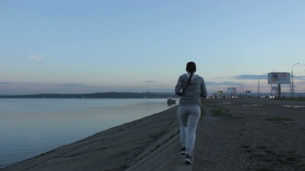 Une fille en jogging du soir. Jeune femme courant dans la ville sur le barrage, près de l'eau — Video
