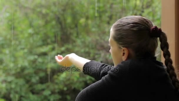 Chica pone su mano bajo la lluvia, tratando de recoger las gotas de lluvia que caen — Vídeos de Stock