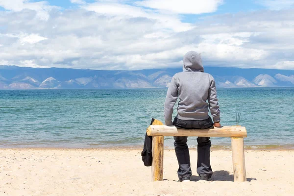 Hombre o mujer está sentado en una sudadera con capucha en la playa. Vista trasera Imágenes de stock libres de derechos
