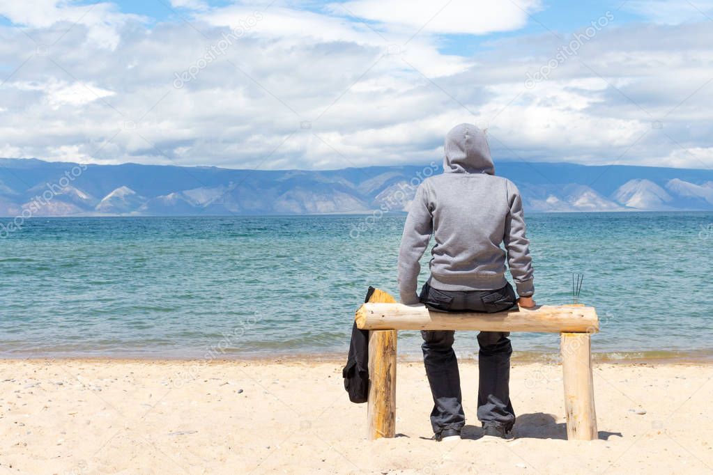 Man or woman is sitting in a hoodie on the beach. Back view