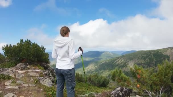 Mulher com postes de trekking fica no topo da montanha e contempla paisagens — Vídeo de Stock