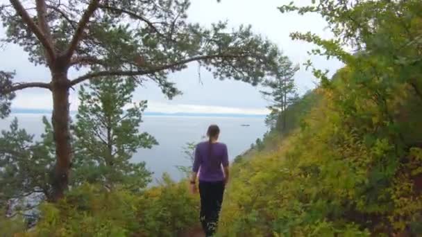 Dziewczyna wspina się po ścieżce na stromym zboczu wybrzeża jesienią — Wideo stockowe