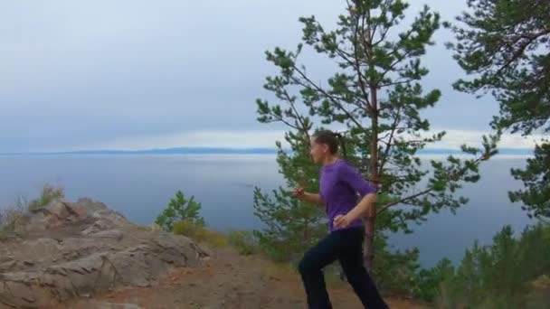 Fille court vers le haut de la falaise, saute et lève les mains — Video