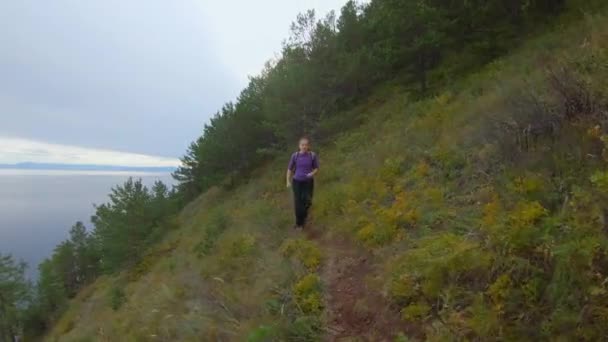 Dívka s batohem běží po stezce na strmém vysokém svahu pobřeží — Stock video
