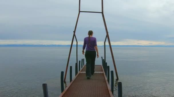 Meisje loopt langs een metalen pier op een bewolkte dag. Langzame beweging, volg schot — Stockvideo