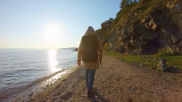 Chica con mochila camina en la orilla del mar al atardecer — Vídeo de stock