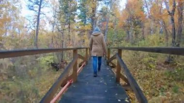Girl in a hood walks along an eco trail in the autumn forest