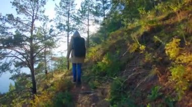 Kapüşonlu ve sırt çantalı bir kız güneşli bir günde dik yamaçta yürüyor.