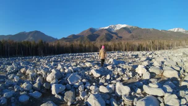 Una chica camina por un campo lleno de grandes rocas. Movimiento lento — Vídeos de Stock