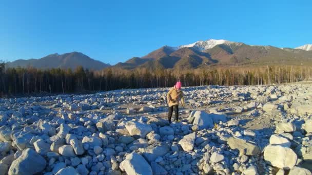Κορίτσι περπατά μέσα από ένα χωράφι με μεγάλες πέτρες. Ορεινό τοπίο στο παρασκήνιο — Αρχείο Βίντεο