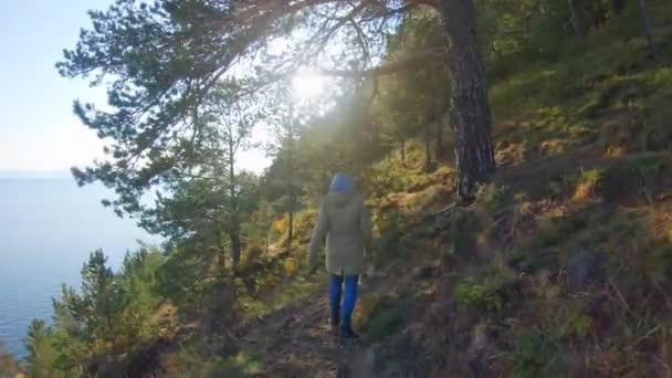 在阳光明媚的日子里，头戴风帽的女孩沿着陡峭的海滨散步 — 图库视频影像
