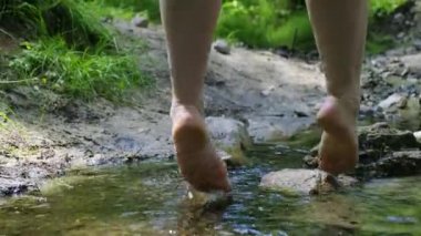 Kız derenin üzerindeki tahta köprüde oturur ve çıplak ayaklarıyla suda sallanır.