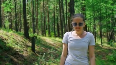 Mavi gözlüklü kız yeşil ormanda yürüyor. Yavaş çekim, 4K