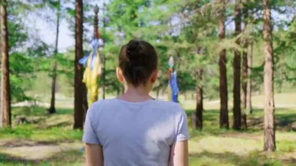 Une fille passe entre deux pôles avec des rubans colorés dans la forêt. Vue arrière, 4K — Video