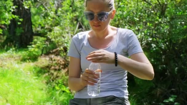 Chica descansa y bebe agua sentada en el tronco en el bosque en verano en el día soleado — Vídeos de Stock