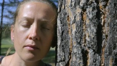 Kapalı gözlü bir kızın portresi, başını ağaca yaslıyor.