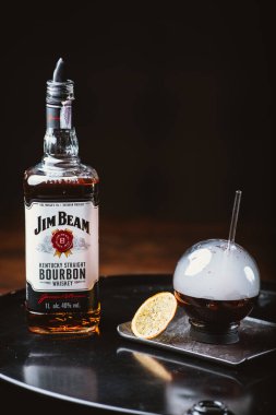 Odessa, Ukrayna - 7 Şubat 2020: Jim Beam en çok satan burbon markalarından biridir. Dumanlı alkol. Jim Beam şişesi siyah arka planda küresel gözlüklerle düzenlenmiş..