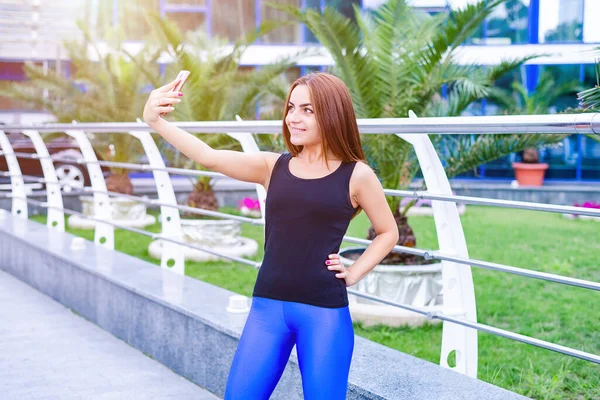 Parkta durup egzersiz yaptıktan sonra selfie çeken genç ve güzel bir sporcu..