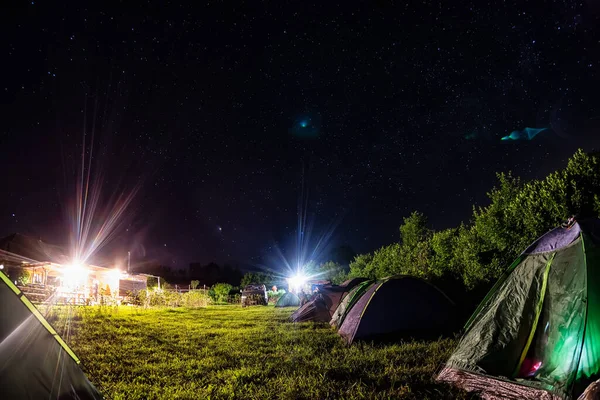 Night camping under starry sky. Glowing tourist tent, under beautiful evening sky full of stars and Milky way, city lights on background. Outdoor lifestyle concept — Stock Photo, Image