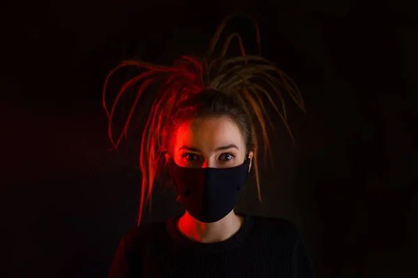 A girl in a mask on a black background. Title about the outbreak of the corona virus in China, illness. Epidemic. Girl with a black mask on her face against coronavirus disease