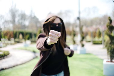 Tıbbi maskeli ve gözlüklü agresif kız saldırıyor. Koronavirüs karantinası sırasında soygun. Odaklanamayan geçmişine yumruk atan genç kız..