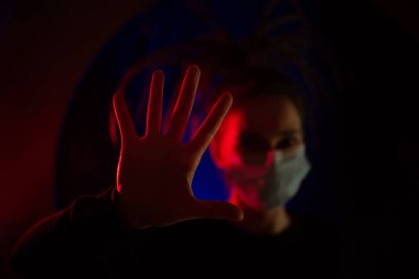 Covid-19 virüsünü durdurun. Eller Sağlıklı. Sıhhiye maskesinde, odağını kaybetmiş bir şekilde. Karanlık bir odada kırmızı ve mavi ışığı olan bir sağlıkçı kız. Coronavrus salgını sırasında.