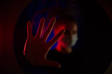 Sıhhiye maskesinde, odağını kaybetmiş bir şekilde. Karanlık bir odada kırmızı ve mavi ışığı olan bir sağlıkçı kız. Coronavrus salgını sırasında. Eller Sağlıklı.