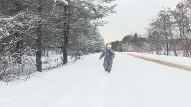 Kış ormandaki küçük çocuk kameraya doğru kar üzerinden çalışır.