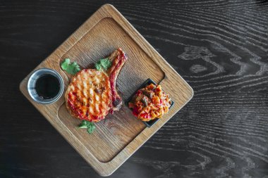 Kesme tahtasında servis edilen kızarmış bifteğin en üst görüntüsü siyah ahşap arka planda sosla servis ediliyor.