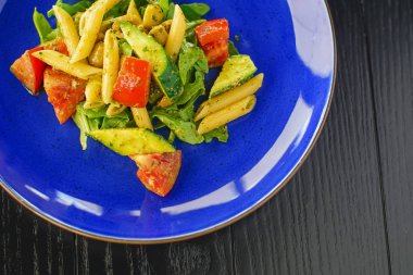 Vejetaryen sebze kepekli kepekli makarna. Mavi tabakta, siyah ahşap arka planda..