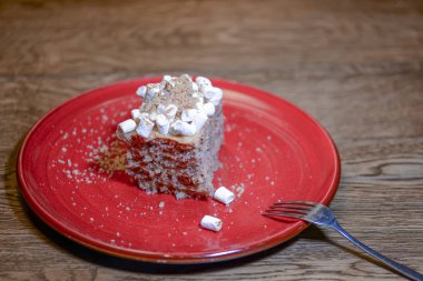 Ekşi kremalı çikolatalı pasta, jöle ve marşmelov ahşap bir masada kırmızı bir tabakta servis edilir..