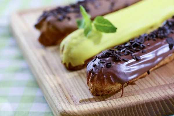 Traditional french dessert eclair pastry, three pieces laying on wooden board on a table covered with plaid fabric.