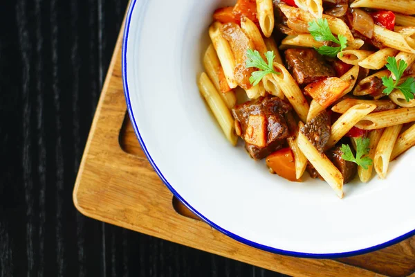 Etli, sebzeli geleneksel İtalyan makarnası ve siyah ahşap arka planda beyaz tabakta maydanoz.