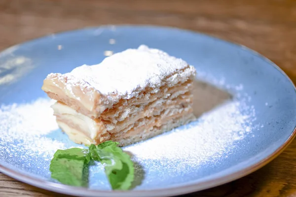 Layered cake with cream Napoleon, vanilla slice with mint and sugar powder served on blue plate on wooden table. — Stock Photo, Image