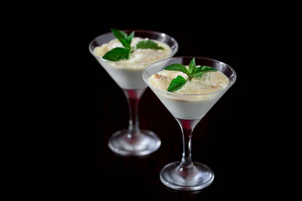 Two glasses of sweet milk dessert with coconut, peanuts and mint on black background with copy space