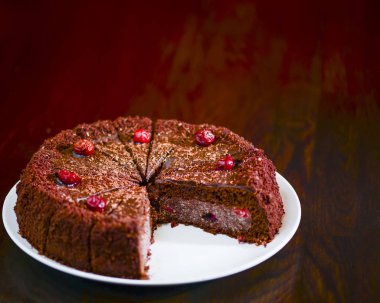 Koyu ahşap masada beyaz tabakta servis edilen kırmızı kirazlı çikolatalı pasta..