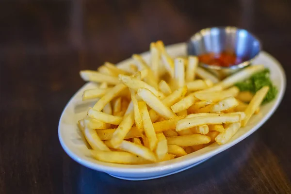 Servieren von Pommes mit Tomatensauce auf weißem Teller auf dunklem Holzhintergrund — Stockfoto