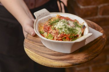 Garson bir tabak lezzetli yemek tutuyor. Restoranda İtalyan mutfağı, soslu makarna, parmesan peyniri ve sebze.