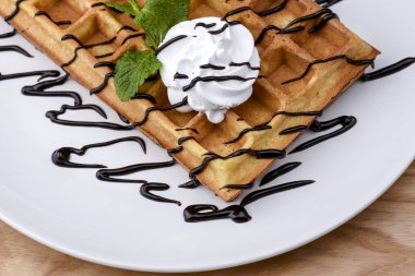 Bir tabak Belçika waffle 'ı dondurmalı tatlı ve ahşap masa arkasında çikolata karamelli sos..