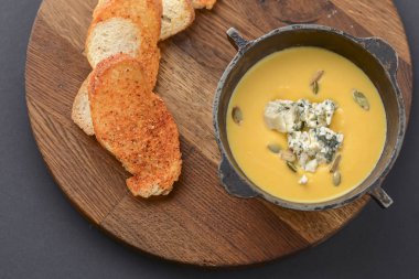 Kabak tohumlu balkabağı çorbası ve ahşap kesim tahtasındaki bir kasede ekmekle servis edilen mavi peynir.