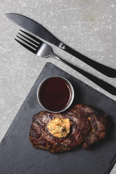 Bife grelhado médio raro com molho em tábua de corte de madeira preta com utensílios. Espaço de cópia, flat lay . — Fotografia de Stock