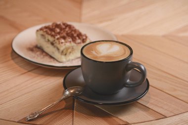 İtalyan usulü tatlı, beyaz tabakta bir parça Tiramisu keki ve siyah bir fincanda siyah bir kahve.