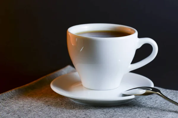 Fehér csésze fekete tea tálalva egy tányéron kanállal sötét asztal háttér. Forró ital. — Stock Fotó