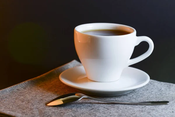 Fehér csésze fekete tea tálalva egy tányéron kanállal sötét asztal háttér. Forró ital. — Stock Fotó
