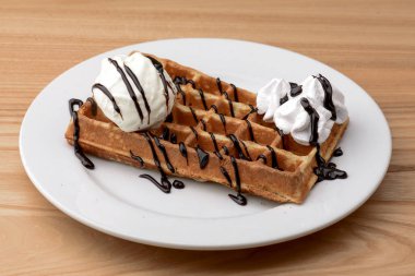 Bir tabak Belçika waffle 'ı dondurmalı tatlı ve ahşap masa arkasında çikolata karamelli sos..